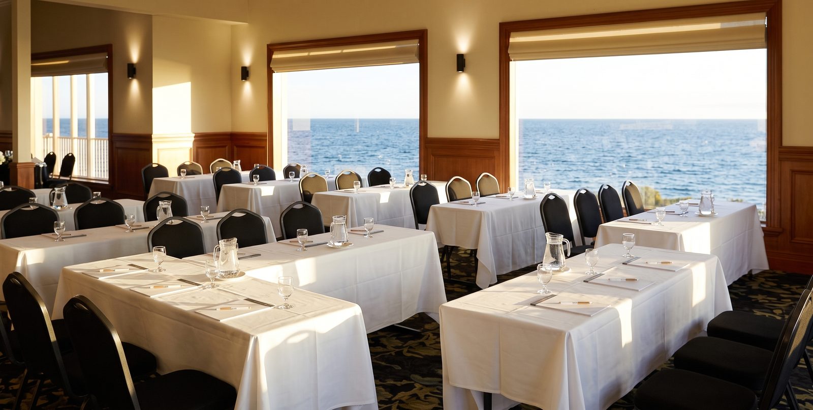 The Bayview Room at the Brighton Beach Hotel set up classroom-style, rows of tables and black chairs facing big windows over Port Phillip Bay (digitally restyled)